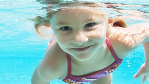 Young girl under water smiling while swimming