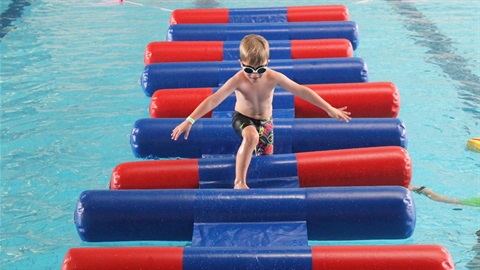 Child running across inflatable obstacle course in swimming pool