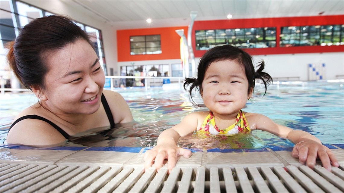 Mother supporting young daughter on the edge of swimming pool