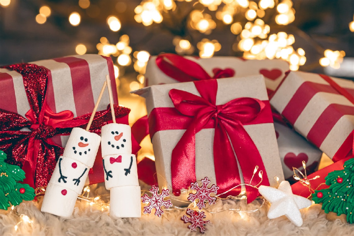 Christmas gift boxes on the floor with smiling marshmallows and a Christmas tree at the back with lights. 